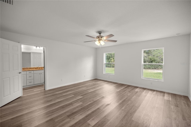 unfurnished bedroom with multiple windows, wood-type flooring, connected bathroom, and ceiling fan