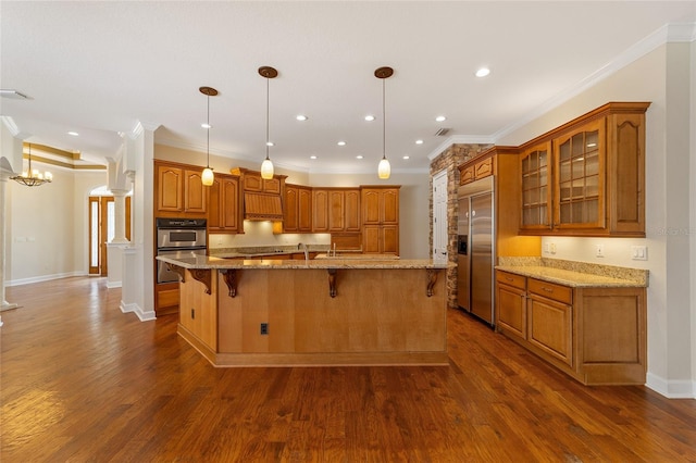 kitchen with an island with sink, dark wood-type flooring, hanging light fixtures, and appliances with stainless steel finishes