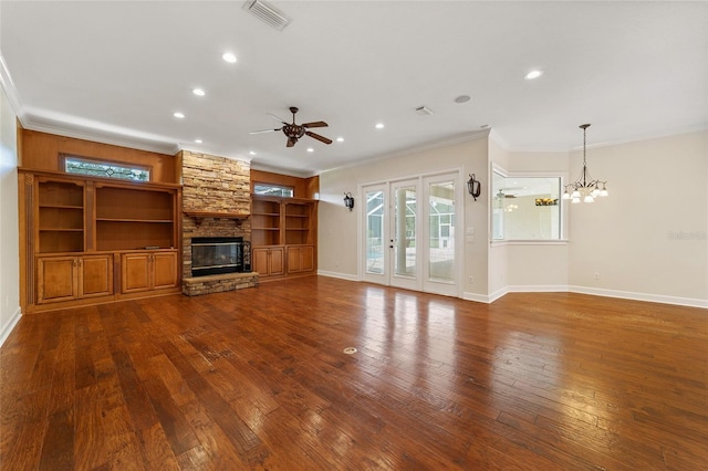 unfurnished living room with ceiling fan with notable chandelier, crown molding, a stone fireplace, and dark hardwood / wood-style floors