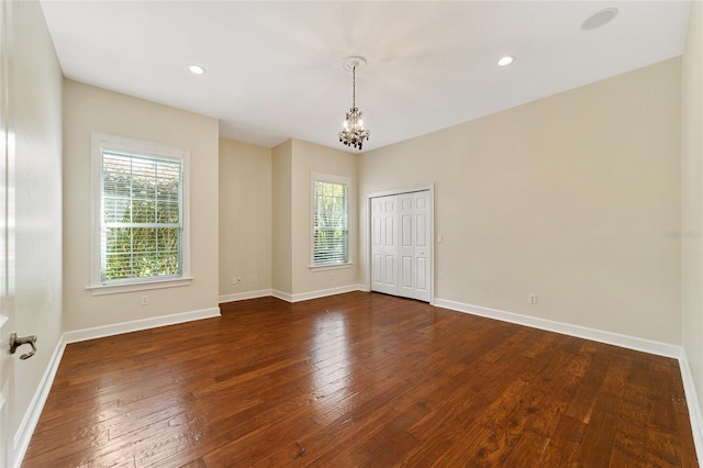 empty room with a healthy amount of sunlight, dark wood-type flooring, and a chandelier