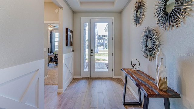 doorway to outside with light hardwood / wood-style flooring, a wealth of natural light, and a raised ceiling