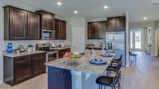 kitchen featuring a kitchen breakfast bar, an island with sink, stainless steel appliances, a textured ceiling, and light wood-type flooring