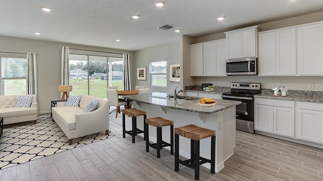 kitchen featuring light hardwood / wood-style flooring, a center island with sink, appliances with stainless steel finishes, and white cabinetry