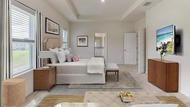 carpeted bedroom featuring a raised ceiling and connected bathroom