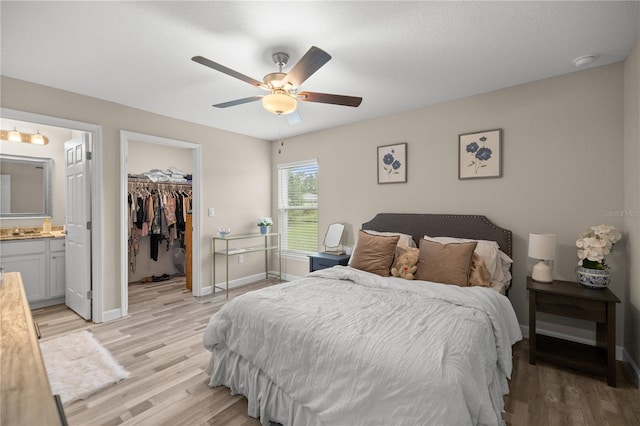 bedroom with light wood-type flooring, ceiling fan, a closet, connected bathroom, and a walk in closet