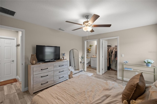 bedroom featuring ceiling fan, light hardwood / wood-style flooring, a spacious closet, a closet, and connected bathroom