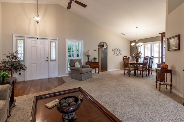 carpeted living room featuring ceiling fan with notable chandelier and high vaulted ceiling