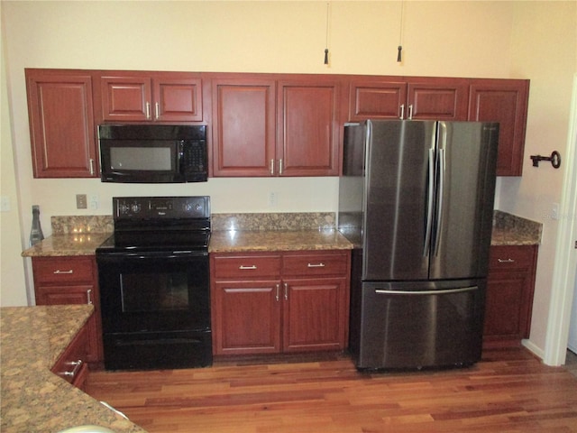 kitchen featuring black appliances, stone counters, and wood finished floors