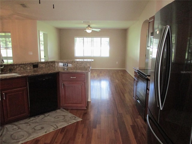 kitchen featuring dark wood-style flooring, a sink, open floor plan, light stone countertops, and black appliances