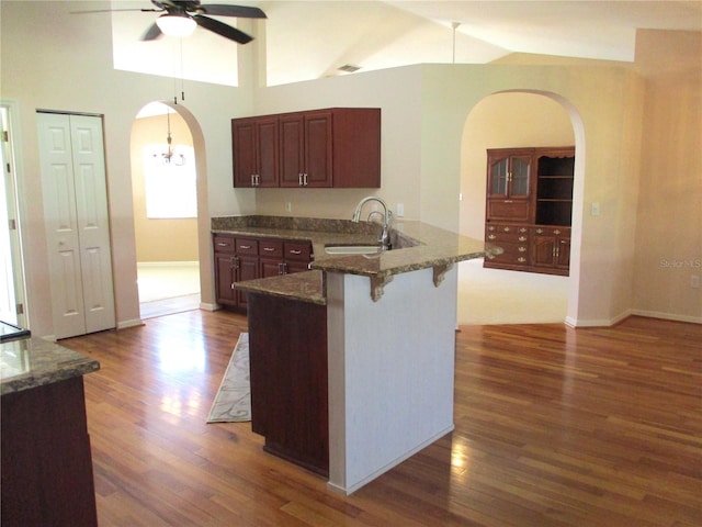 kitchen with arched walkways, a peninsula, dark wood-style flooring, a sink, and a kitchen bar