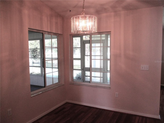 unfurnished dining area featuring a notable chandelier, dark wood-style flooring, and baseboards