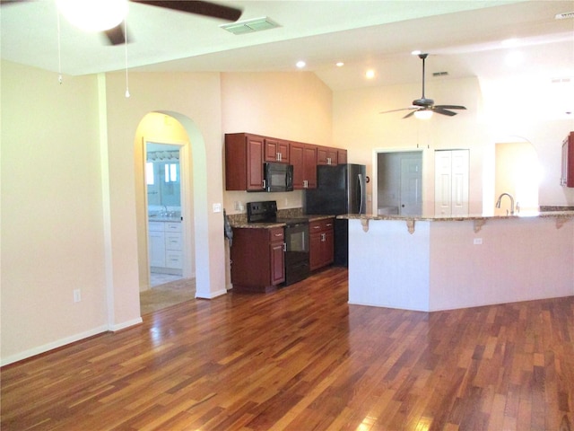 kitchen featuring visible vents, arched walkways, a breakfast bar, dark wood-type flooring, and black appliances