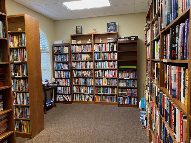 interior space with carpet flooring, wall of books, and a drop ceiling