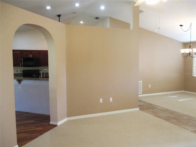 carpeted empty room featuring vaulted ceiling, wood finished floors, ceiling fan with notable chandelier, arched walkways, and recessed lighting