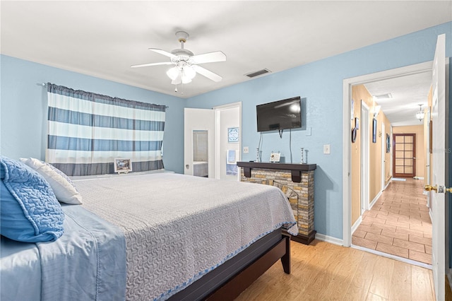 bedroom with hardwood / wood-style flooring, ceiling fan, and a stone fireplace