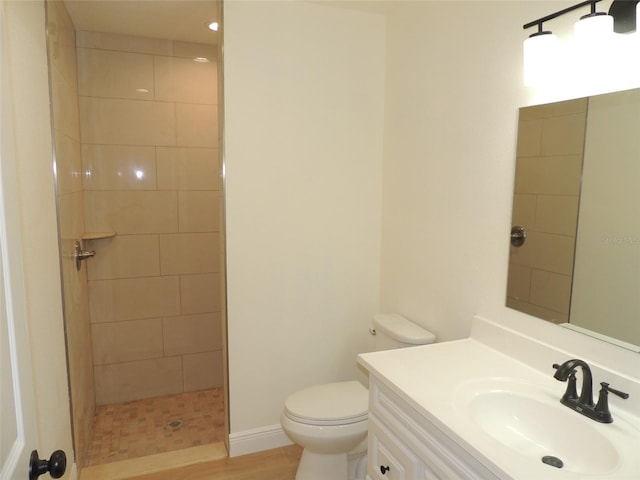 bathroom featuring toilet, vanity, wood-type flooring, and a tile shower