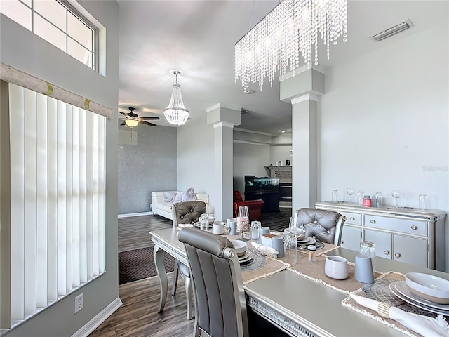 interior space featuring hardwood / wood-style floors, ornate columns, ceiling fan with notable chandelier, a fireplace, and white cabinetry