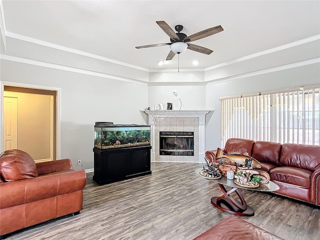 living room with ornamental molding, a tiled fireplace, hardwood / wood-style floors, and ceiling fan