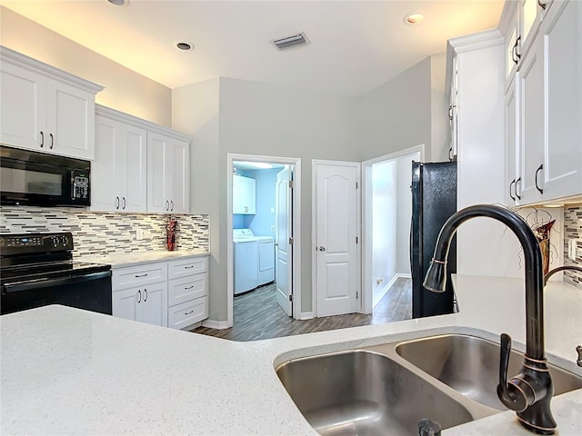 kitchen with hardwood / wood-style floors, sink, washing machine and dryer, black appliances, and white cabinetry