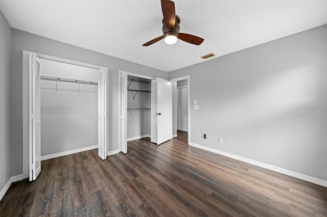 unfurnished bedroom with dark hardwood / wood-style flooring, multiple closets, and ceiling fan