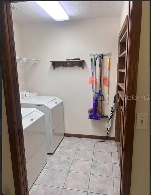 clothes washing area featuring washing machine and clothes dryer, light tile patterned floors, and a textured ceiling