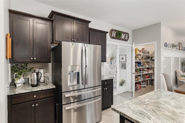 kitchen with light stone counters, dark brown cabinetry, and stainless steel fridge with ice dispenser