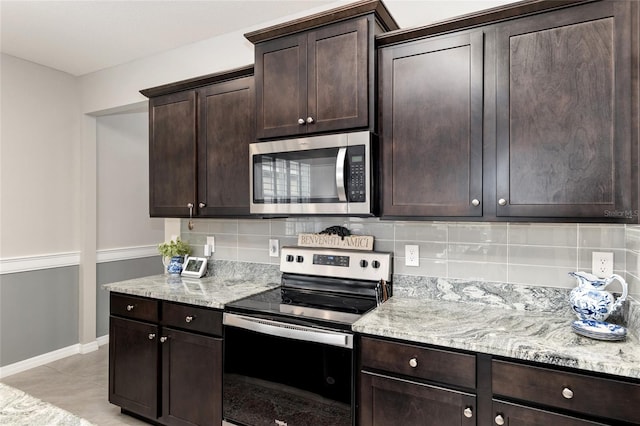 kitchen featuring appliances with stainless steel finishes, light stone countertops, dark brown cabinets, and backsplash