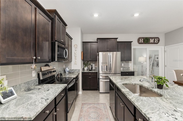 kitchen featuring backsplash, sink, light stone countertops, light tile patterned floors, and appliances with stainless steel finishes