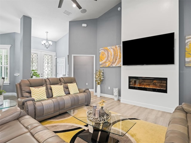 living room with ceiling fan with notable chandelier, high vaulted ceiling, and light hardwood / wood-style flooring