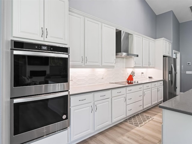 kitchen with decorative backsplash, wall chimney exhaust hood, stainless steel appliances, light hardwood / wood-style flooring, and white cabinetry