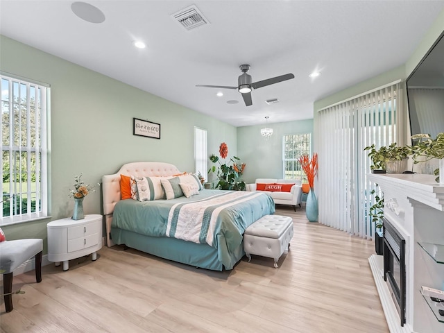 bedroom featuring ceiling fan with notable chandelier, light hardwood / wood-style flooring, and multiple windows