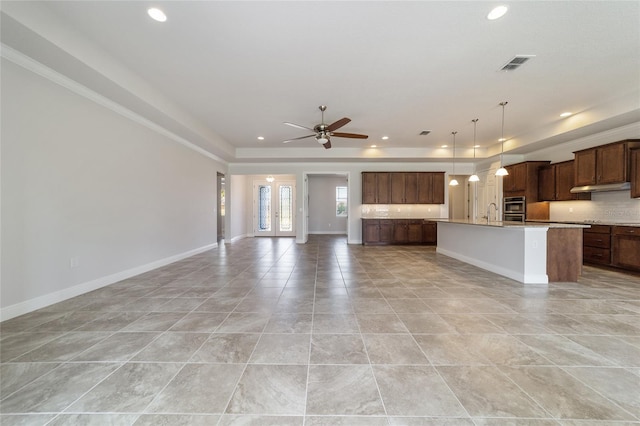 kitchen with ceiling fan, a center island with sink, decorative backsplash, light stone countertops, and hanging light fixtures