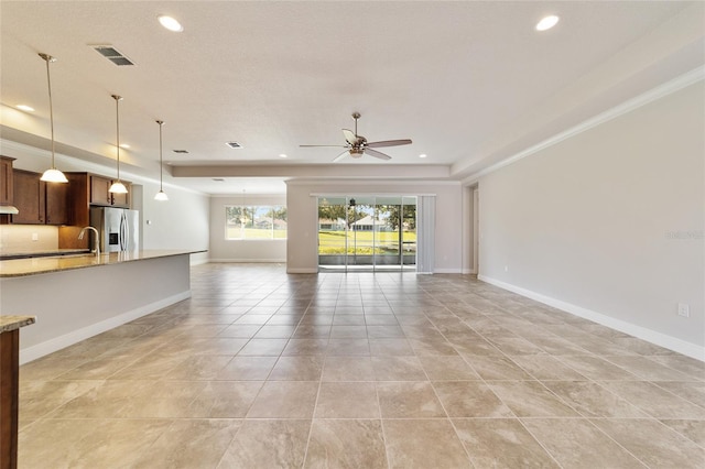 unfurnished living room featuring ceiling fan, light tile patterned floors, ornamental molding, sink, and a tray ceiling