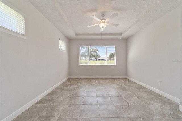 empty room featuring light tile patterned floors, ceiling fan, a raised ceiling, and a textured ceiling