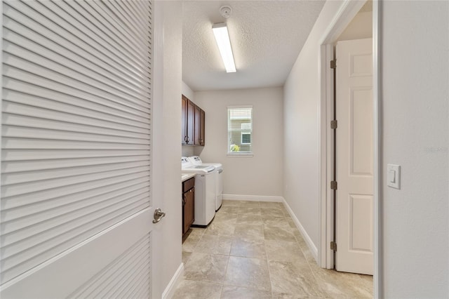 clothes washing area with cabinets, a textured ceiling, and washing machine and clothes dryer