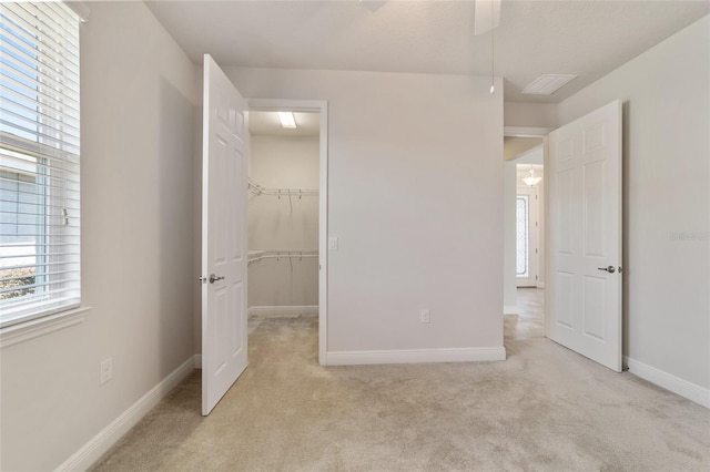 unfurnished bedroom featuring a walk in closet, ceiling fan, a closet, and light colored carpet