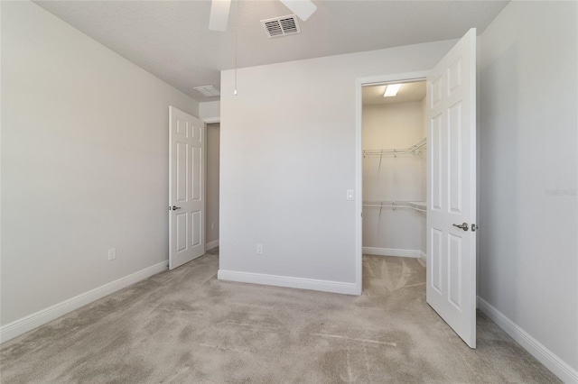 unfurnished bedroom with a spacious closet, ceiling fan, a closet, and light colored carpet