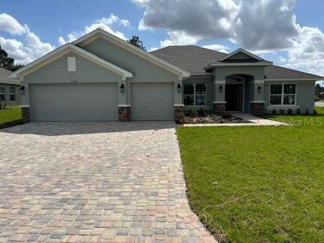 view of front of house featuring an attached garage, stucco siding, a front yard, and decorative driveway