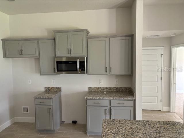 kitchen featuring stainless steel microwave, gray cabinetry, and stone counters