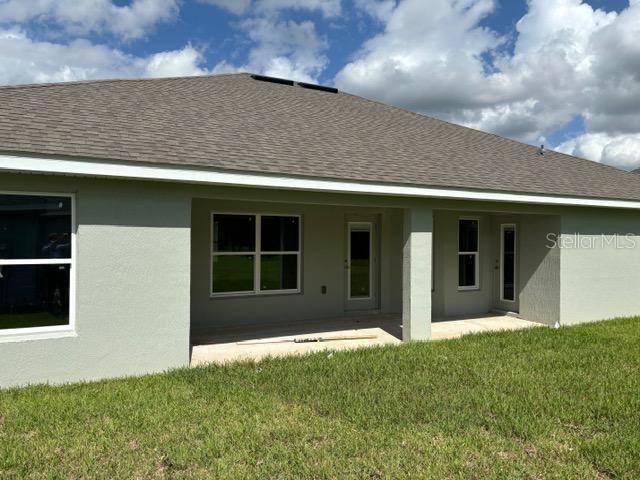 back of house featuring a patio area, roof with shingles, stucco siding, and a lawn