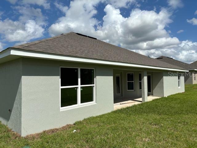 back of property with a patio area, roof with shingles, a yard, and stucco siding