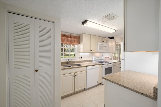 kitchen featuring light stone countertops, white appliances, sink, light tile patterned flooring, and a textured ceiling