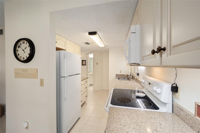 kitchen with white cabinets, white appliances, sink, light tile patterned floors, and a textured ceiling