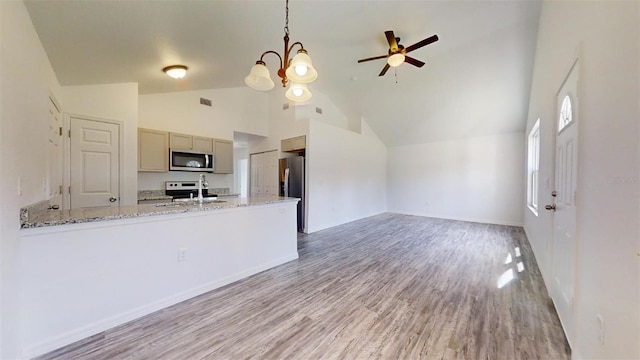 kitchen featuring light stone counters, decorative light fixtures, high vaulted ceiling, stainless steel appliances, and light hardwood / wood-style floors