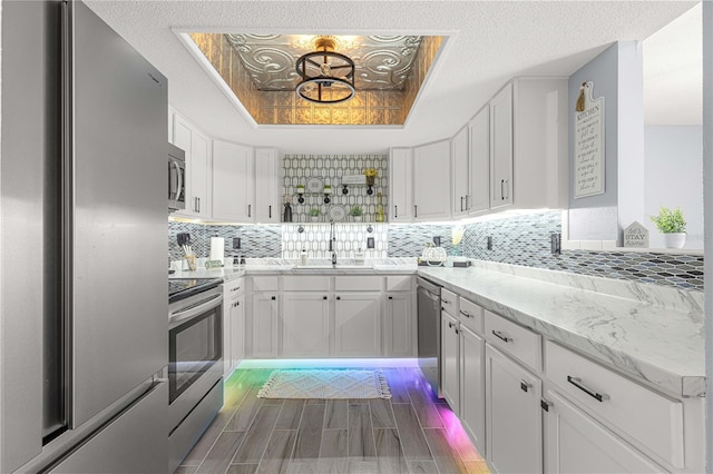 kitchen with white cabinets, a raised ceiling, backsplash, sink, and stainless steel appliances