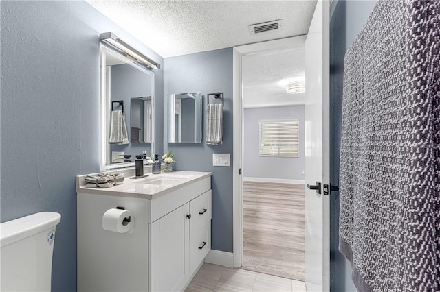 bathroom featuring vanity, toilet, wood-type flooring, and a textured ceiling