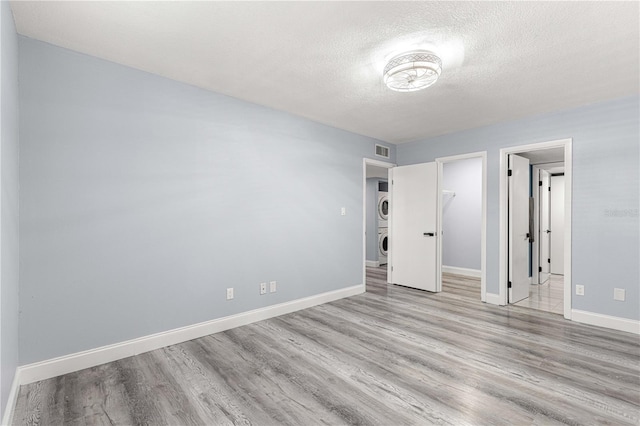 spare room with a textured ceiling, stacked washer and dryer, and light wood-type flooring