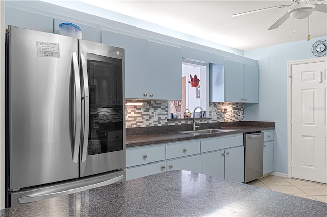 kitchen featuring appliances with stainless steel finishes, sink, blue cabinetry, decorative backsplash, and light tile patterned floors