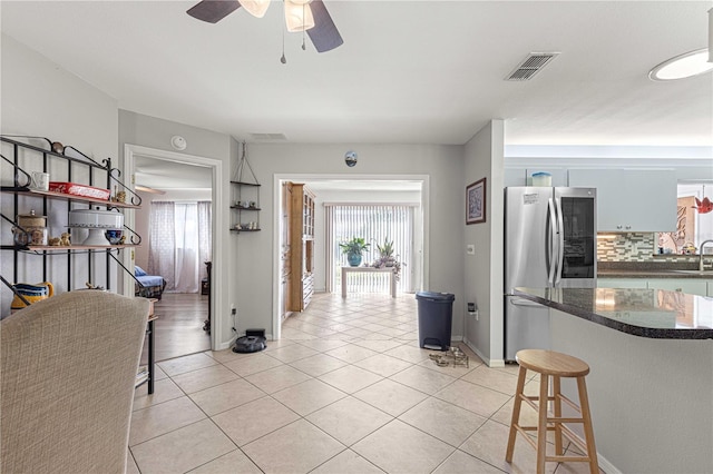 kitchen featuring tasteful backsplash, sink, light tile patterned flooring, stainless steel refrigerator, and a breakfast bar area