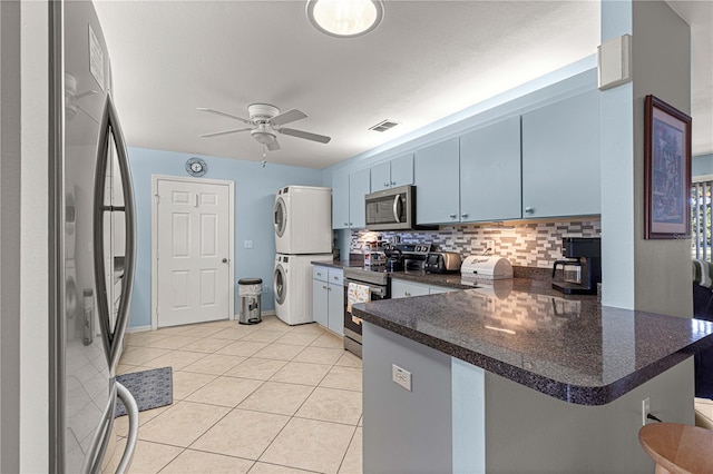 kitchen with appliances with stainless steel finishes, backsplash, kitchen peninsula, blue cabinets, and stacked washer / drying machine